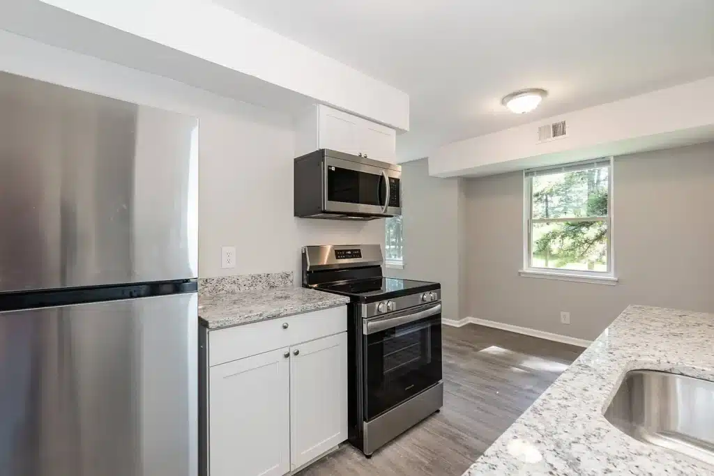 Modern kitchen with stainless steel refrigerator, oven, and microwave, white cabinets, granite countertops, and a window letting in natural light.