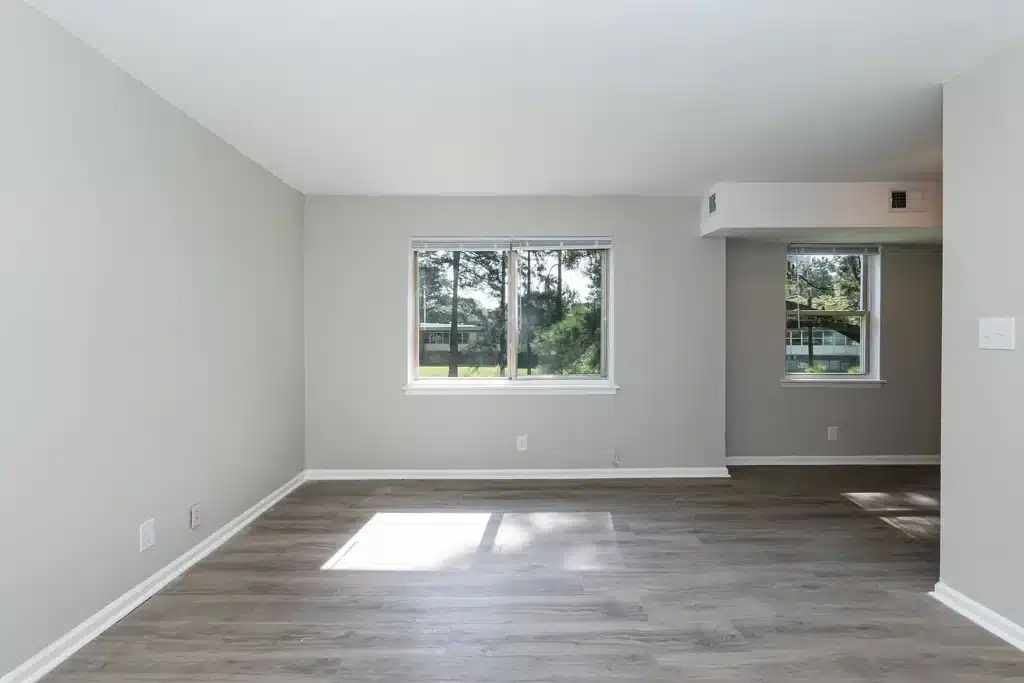 Empty room with light gray walls, wood-look flooring, and two windows letting in natural light. A small section of wall separates the two windows.
