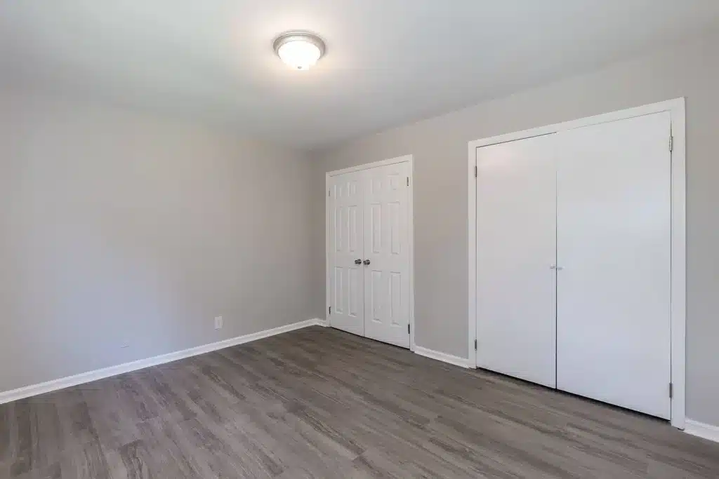 Empty room with light gray walls, wood-look flooring, a ceiling light, and two sets of white double doors.