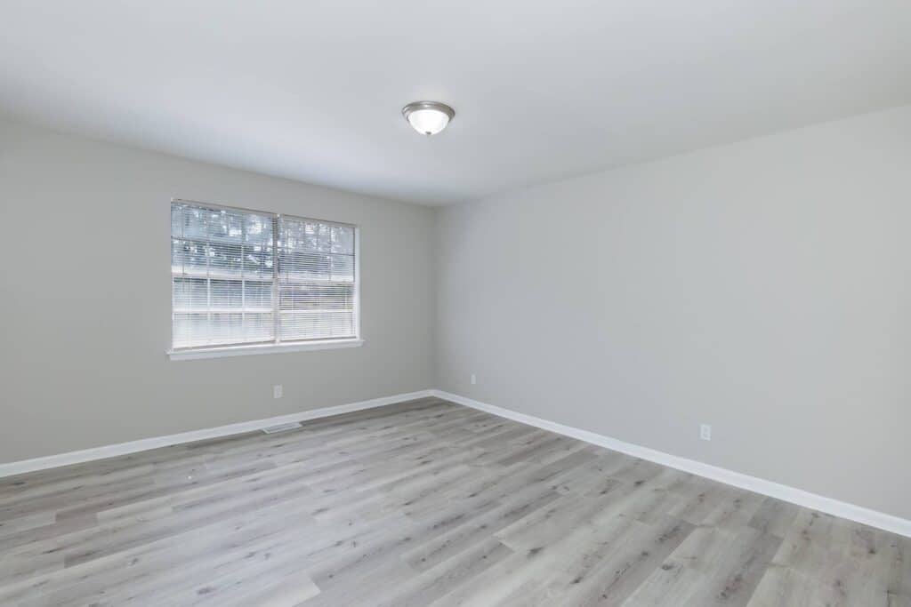 Empty room at Gallery - Delmont Townes with light gray walls, wood-style flooring, a large window with blinds, and a ceiling light fixture.