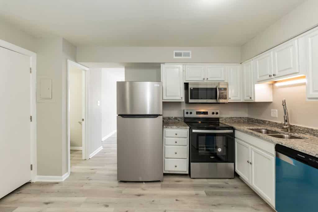 Modern kitchen at Gallery - Delmont Townes features stainless steel appliances, white cabinets, granite countertops, and light wood flooring.