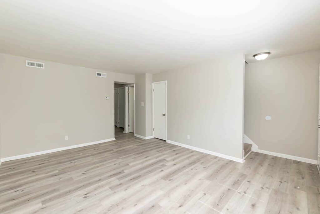 Empty room with light-colored wood flooring, beige walls, a white door, and a staircase leading upward; the space in Gallery - Delmont Townes is well-lit with natural light.